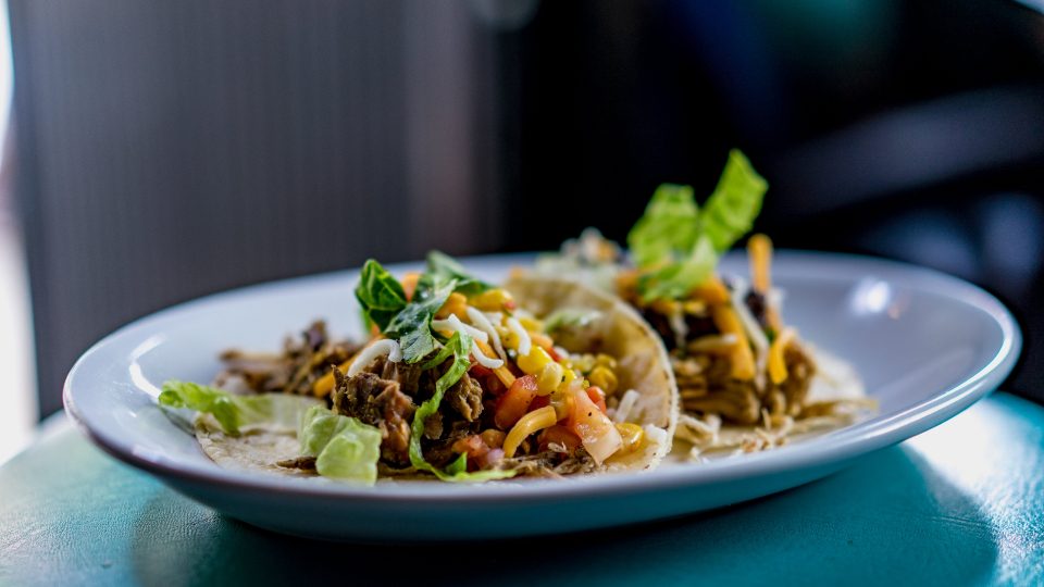 A plate of soft tacos with shredded beef, lettuce, corn salsa and cheese